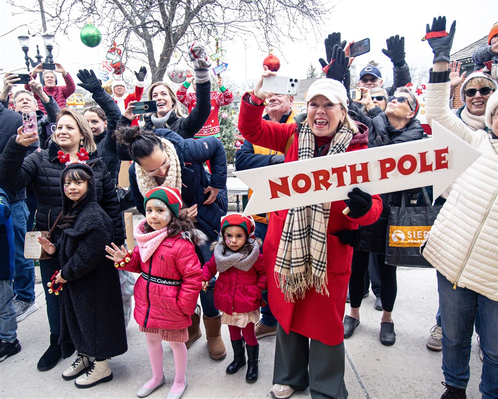 A joyful crowd cheering and holding a North Pole arrow sign