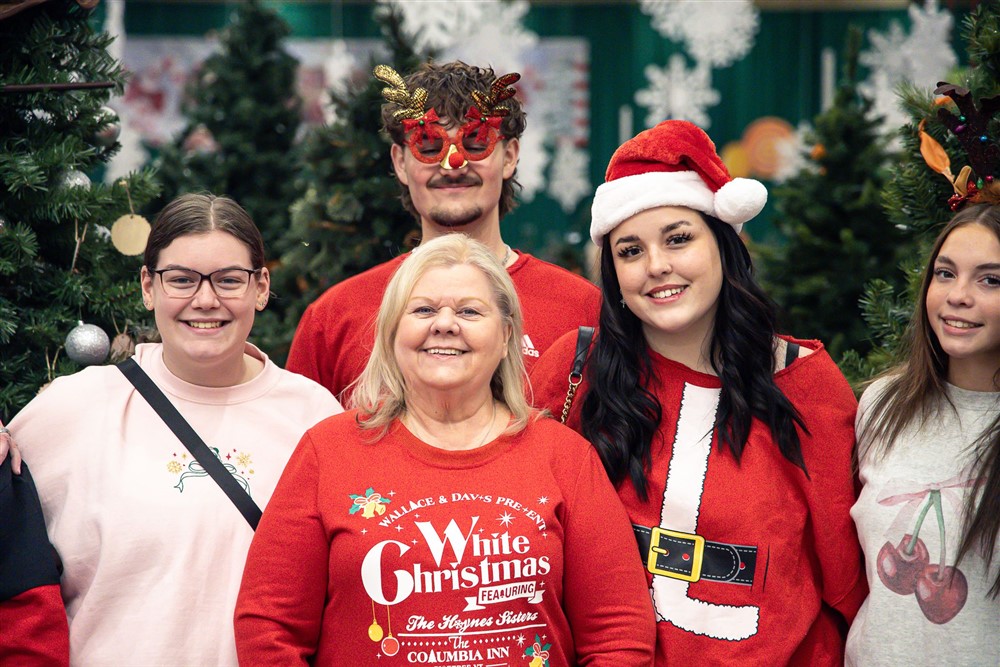 Volunteers in festive holiday attire smiling together in front of Christmas trees
