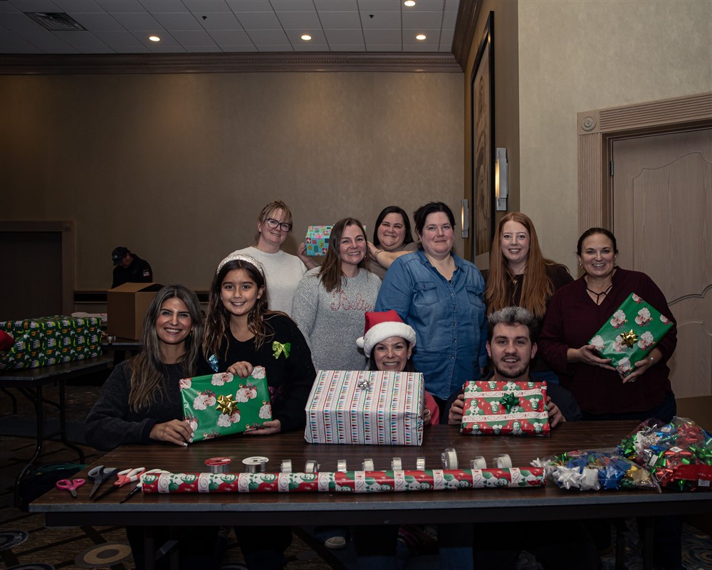 Volunteers smiling together holding brightly wrapped Operation North Pole gifts at a wrapping event